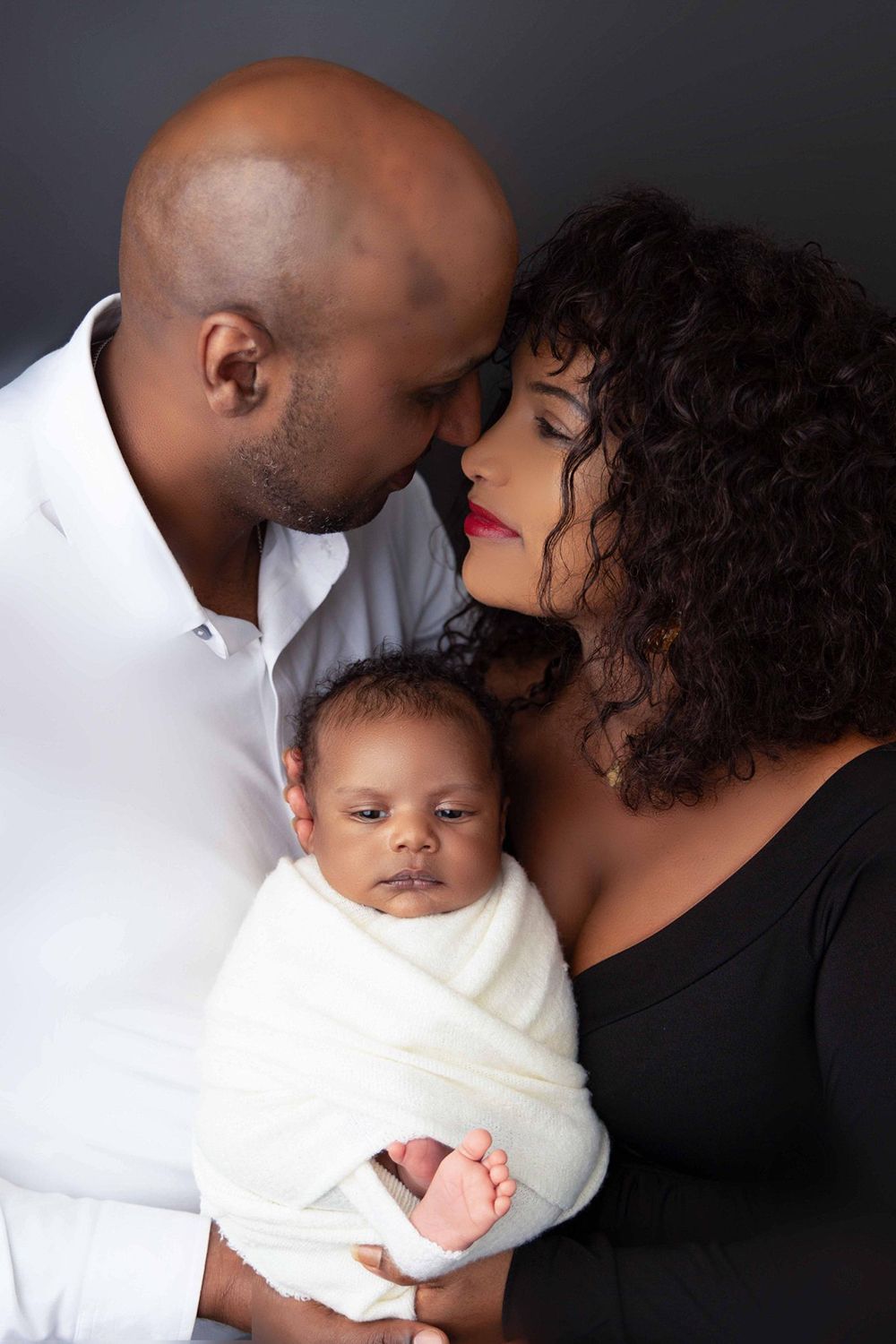 A couple are looking at each other while holding a newborn baby