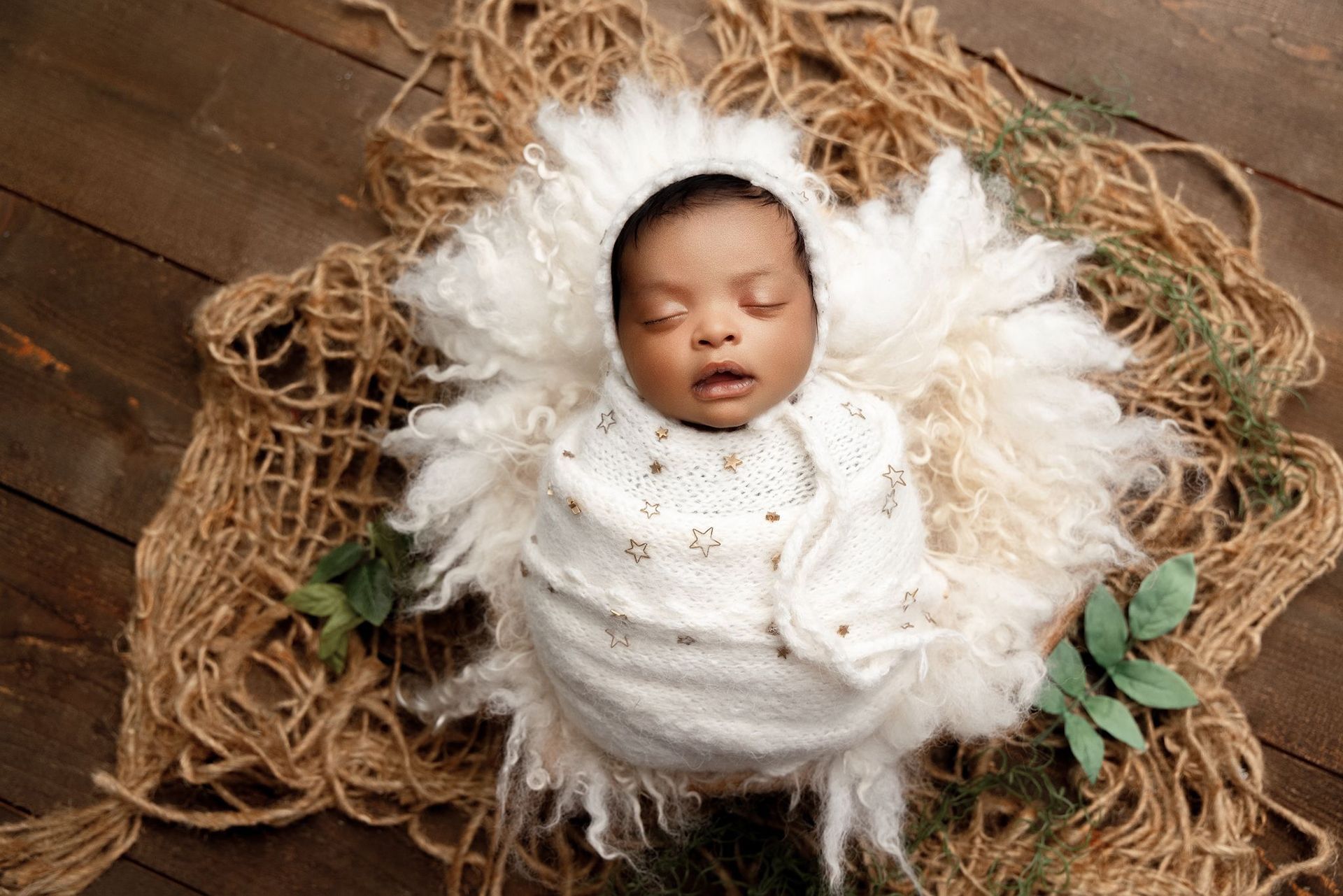 A newborn baby wrapped in a white blanket is sleeping on a wooden floor