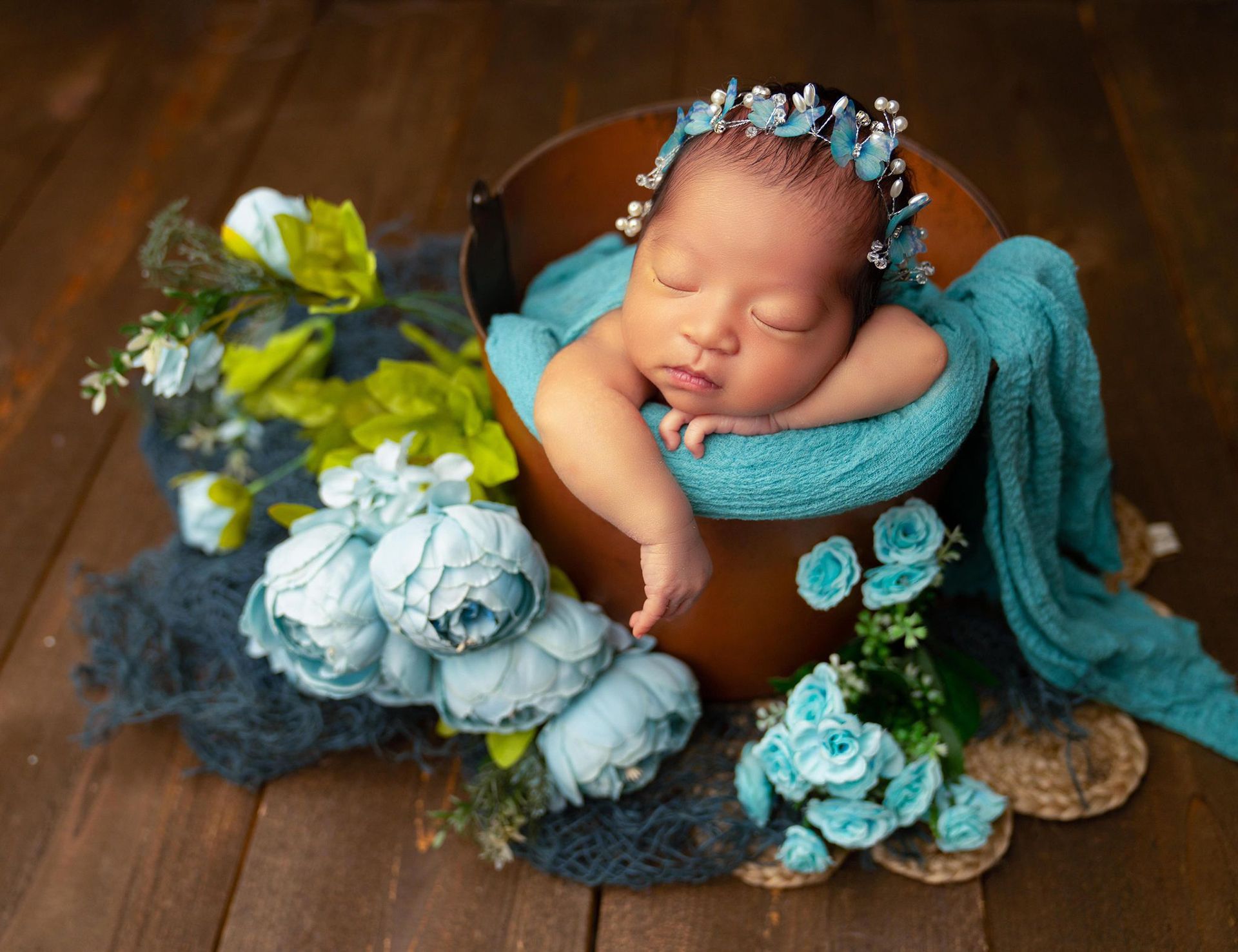 A newborn baby is sleeping in a wooden bucket with blue flowers