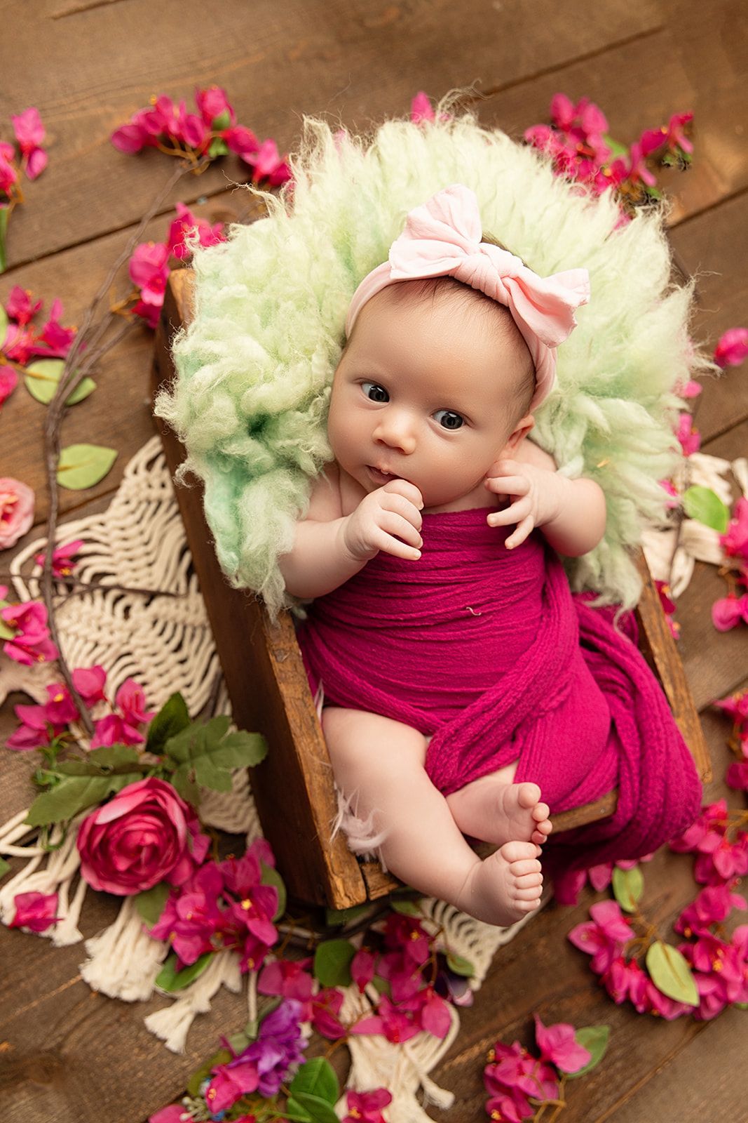 A newborn baby is laying in a wooden crate surrounded by flowers