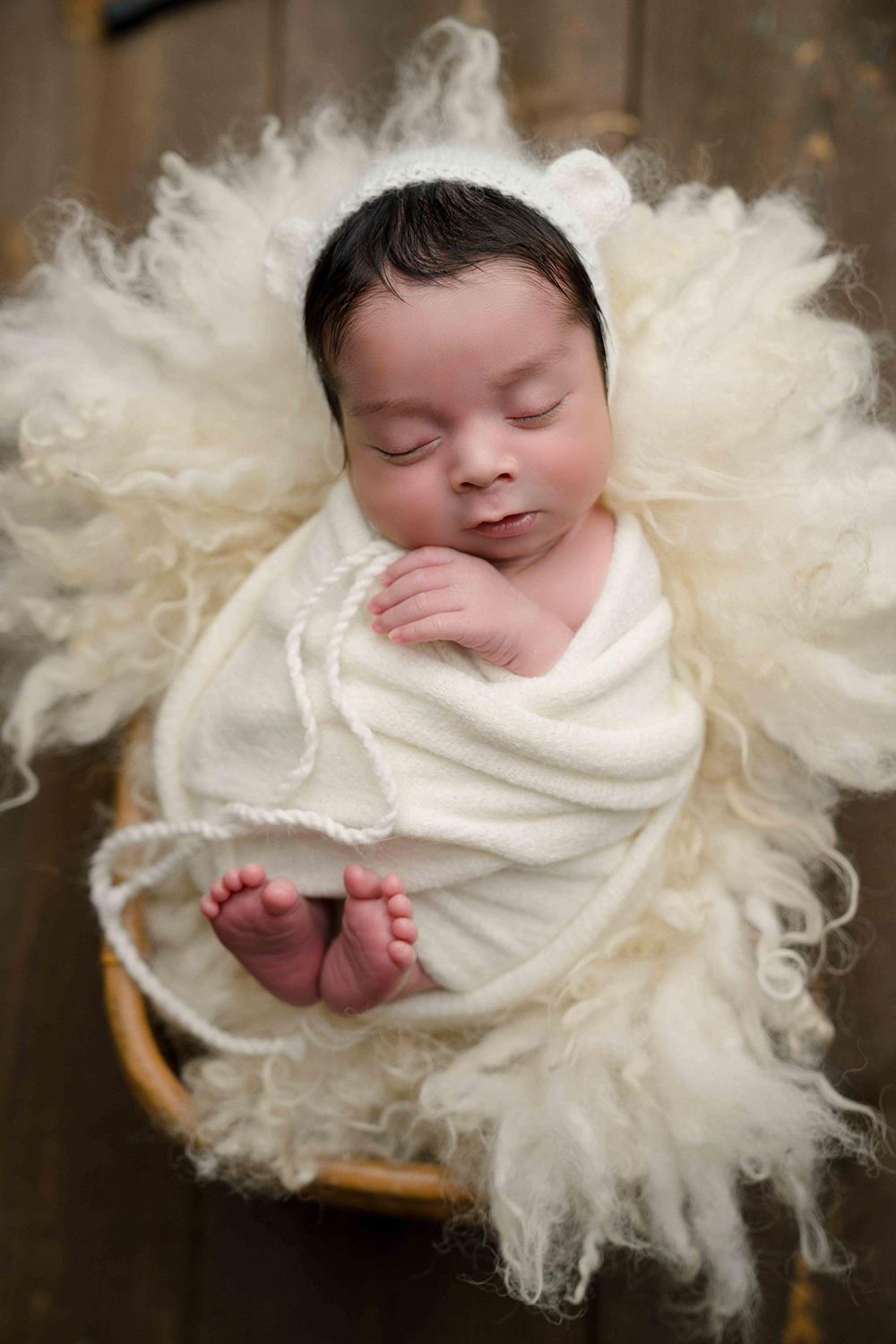A newborn baby wrapped in a white blanket is sleeping in a basket
