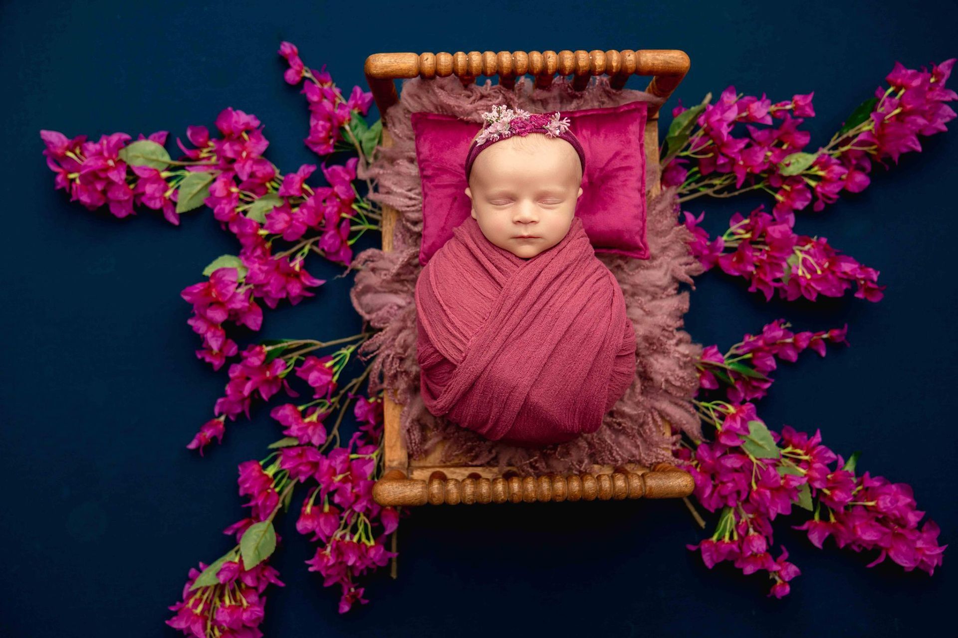 A newborn baby is wrapped in a pink blanket and surrounded by pink flowers