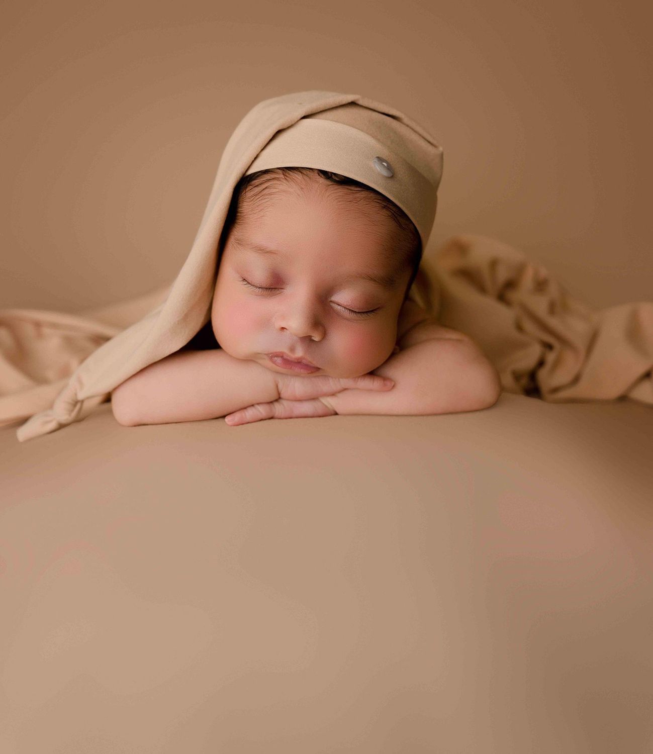 A newborn baby is sleeping on a bed with his head resting on his hands