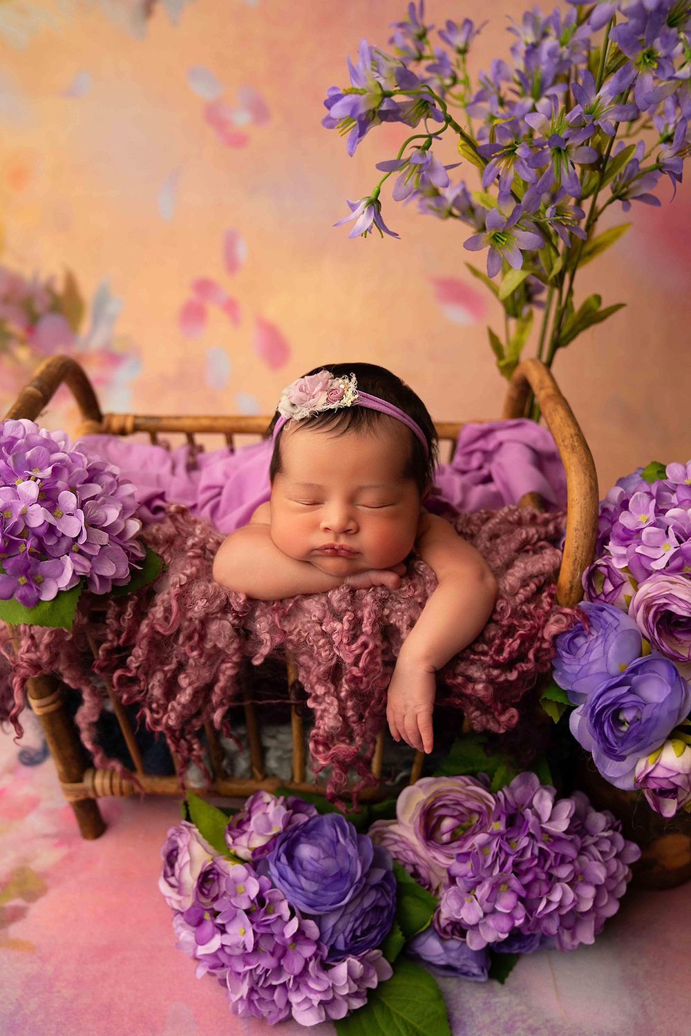 A newborn baby is sleeping in a basket surrounded by assorted flowers