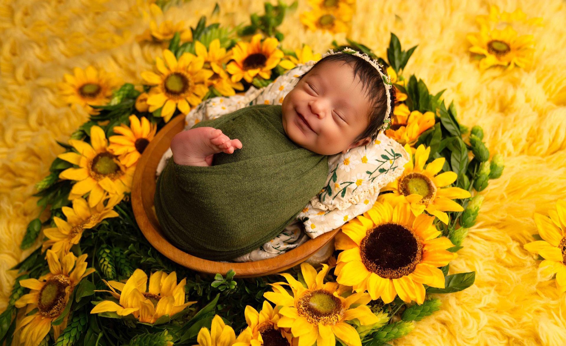 A newborn baby is laying in a bowl surrounded by sunflowers
