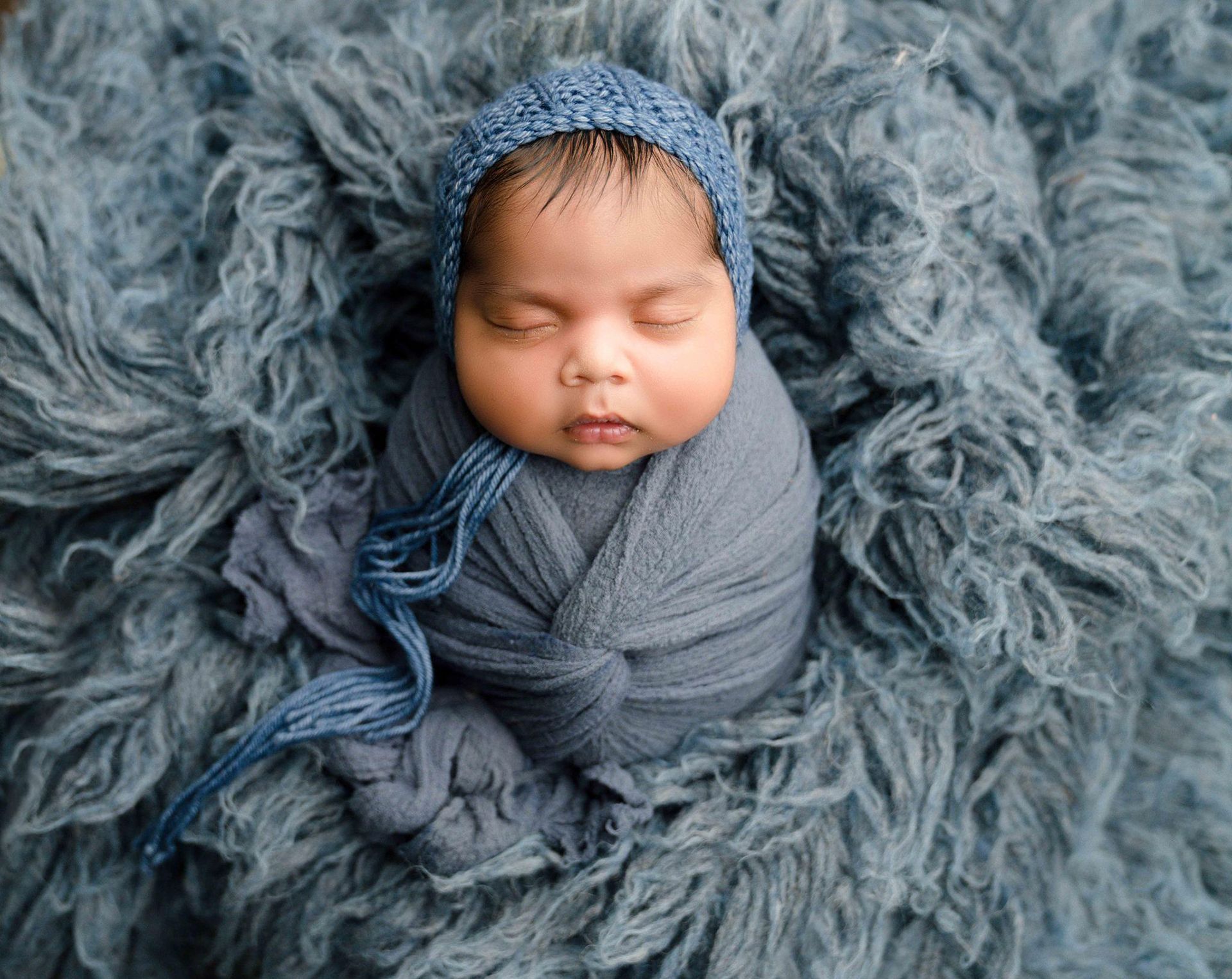 A newborn baby is wrapped in a blue blanket and wearing a blue hat