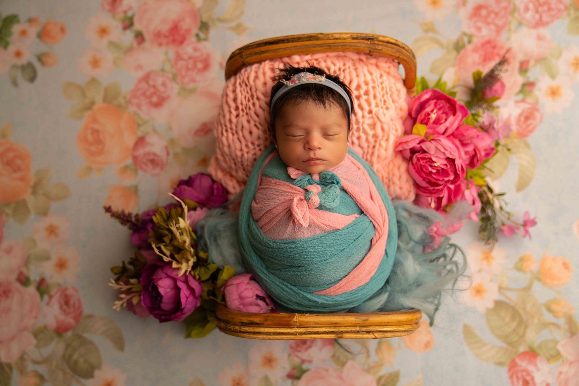 A newborn baby wrapped in a pink and teal blanket