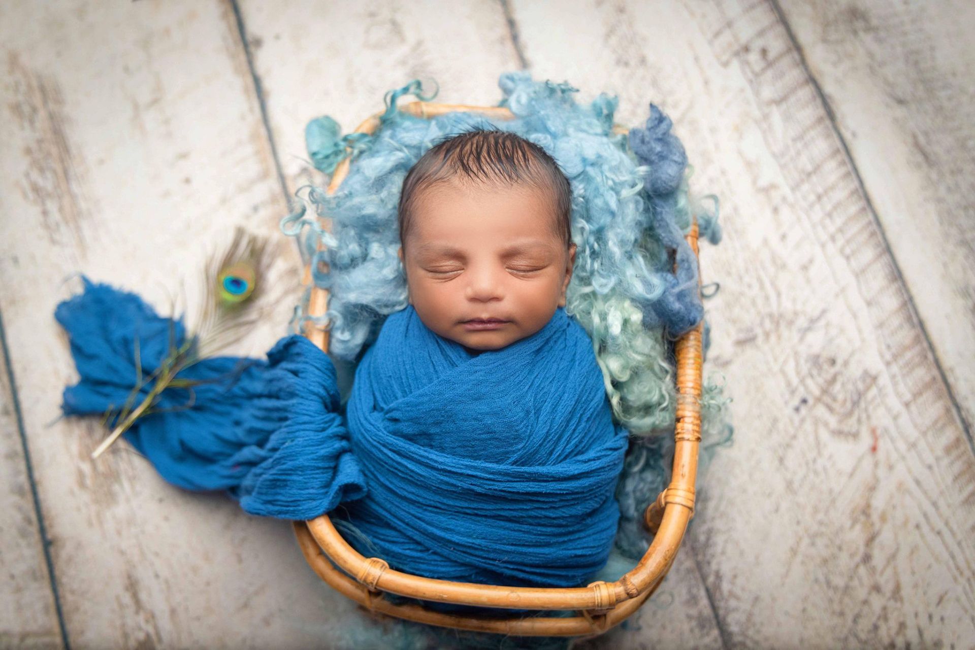 A newborn baby wrapped in a blue blanket is sleeping in a wicker basket