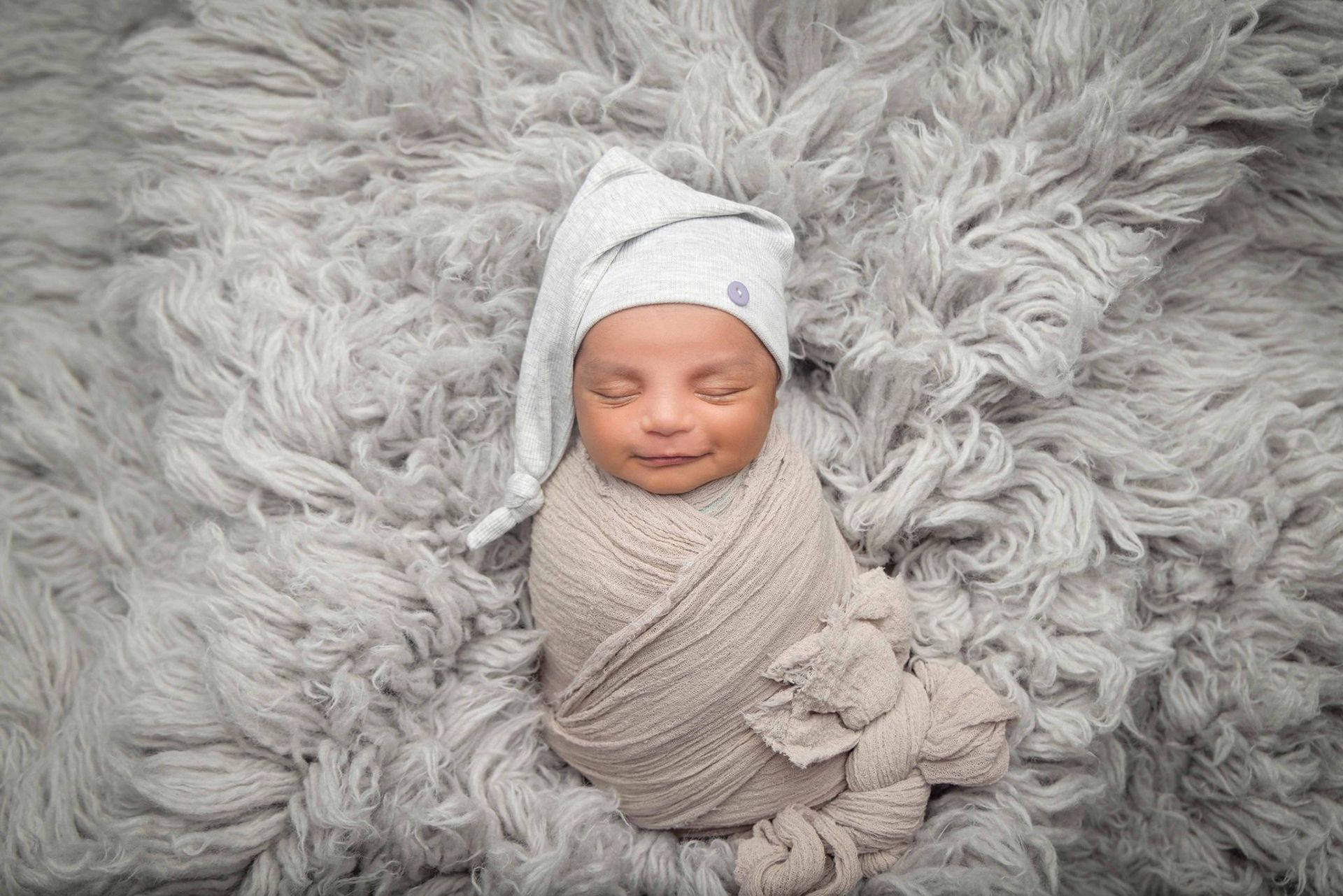 A newborn baby is wrapped in a blanket and wearing a gray hat