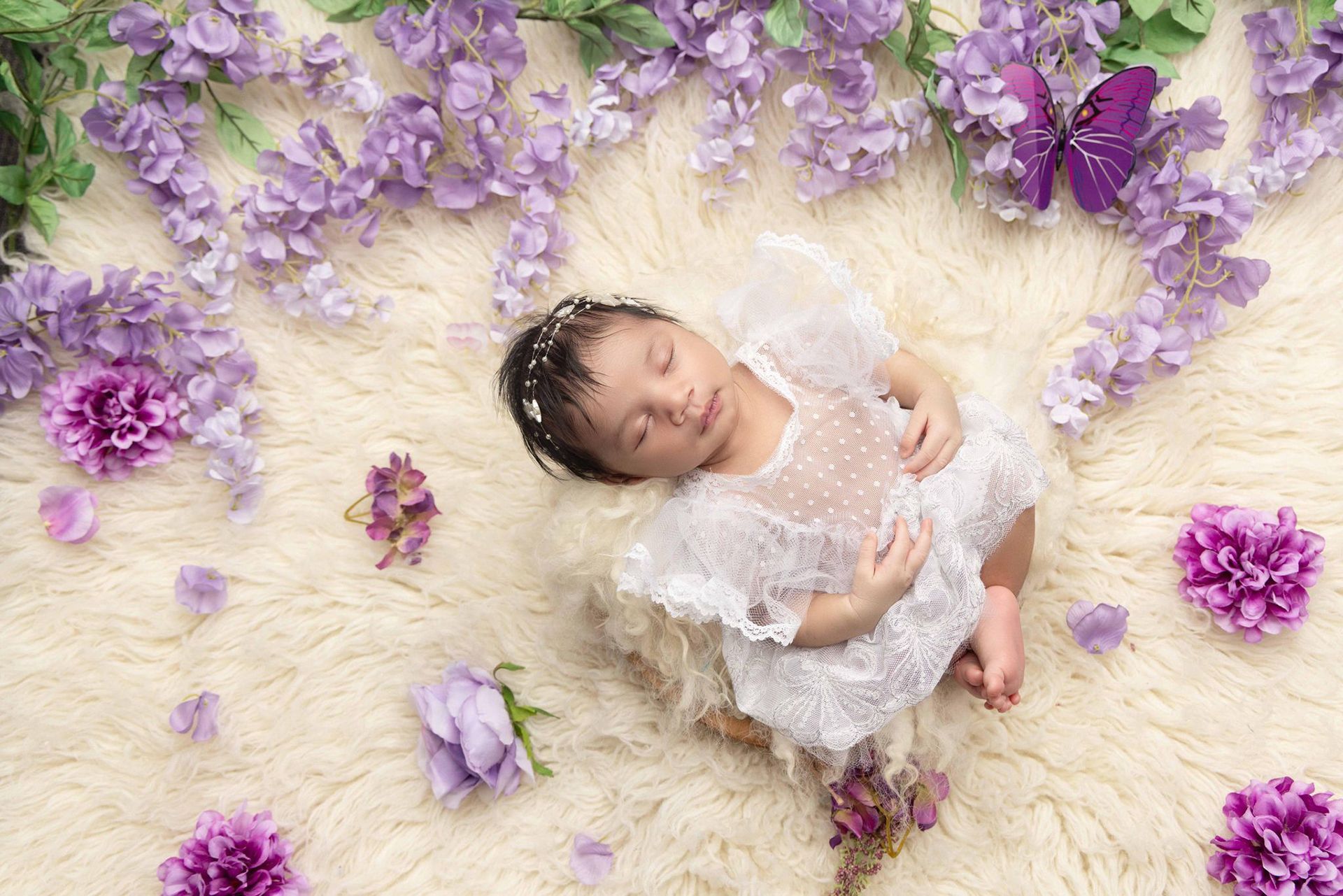 A baby is laying on a blanket surrounded by purple flowers and butterflies