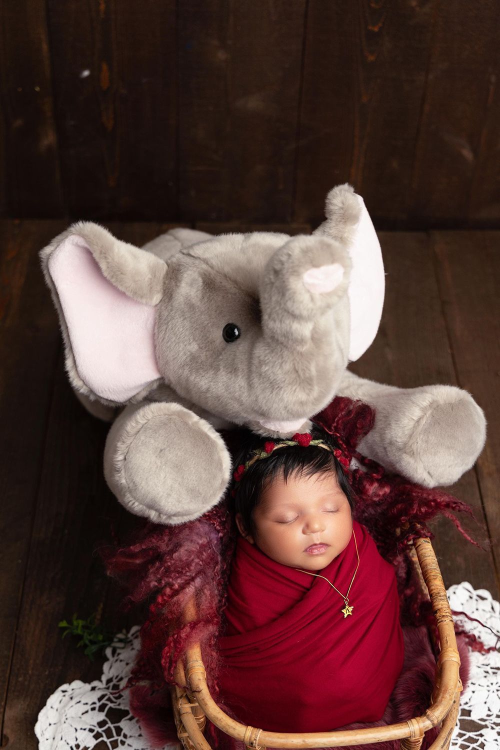 A newborn baby is sleeping in a basket next to a stuffed elephant