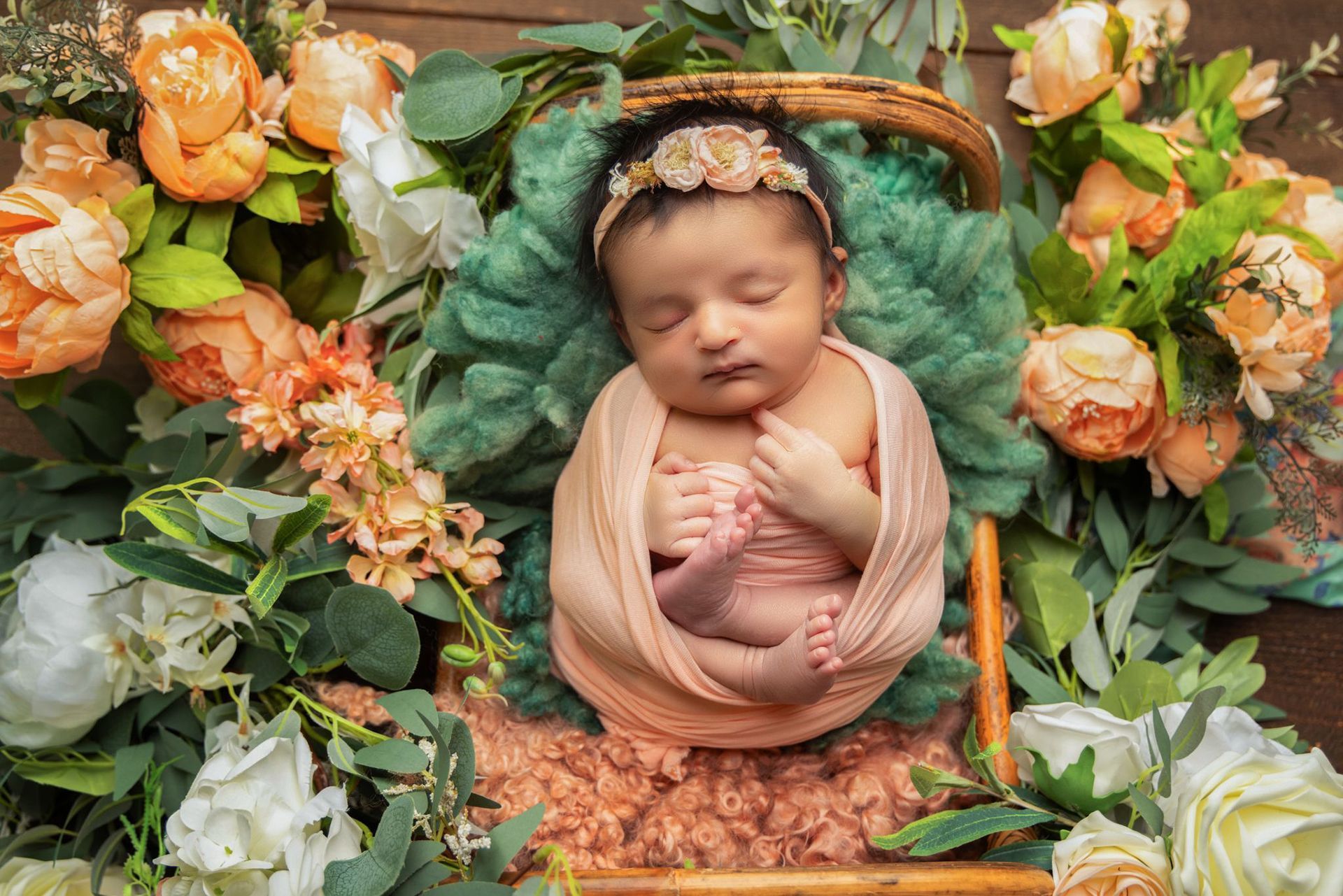 A newborn baby is sleeping in a basket surrounded by peach-colored flowers
