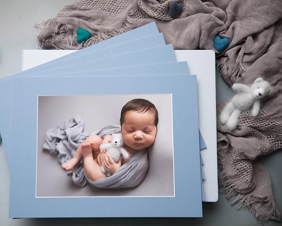 A baby wrapped in a blue blanket is holding a teddy bear