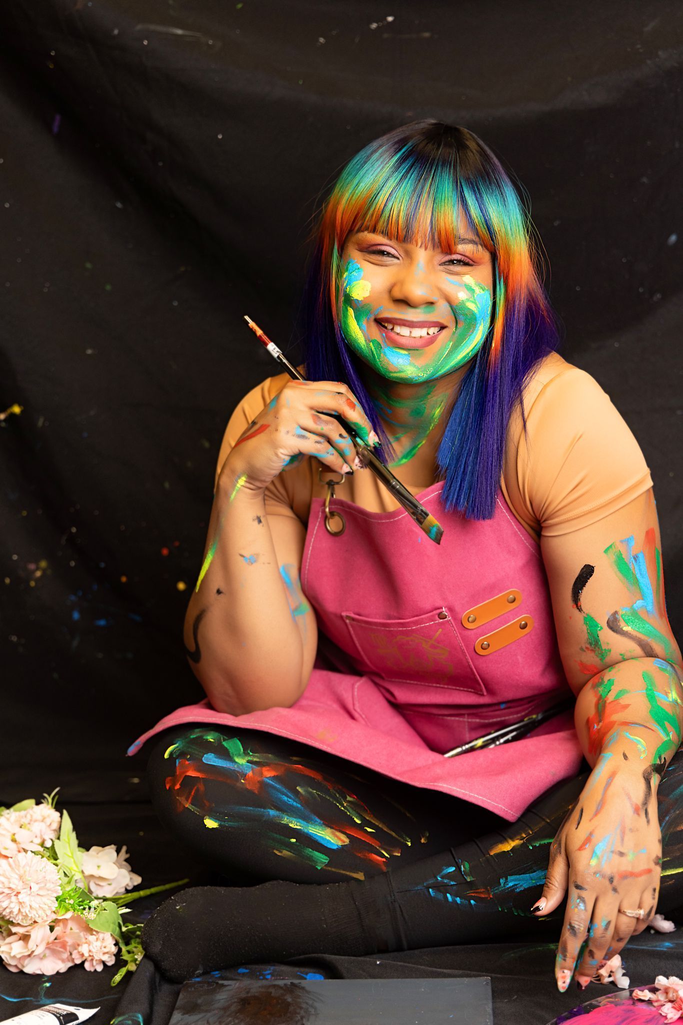 A woman with paint on her face is sitting on the floor holding a brush