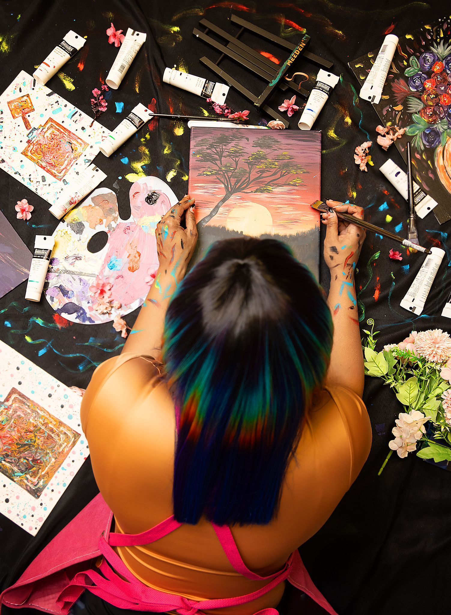 A woman with rainbow hair is painting a picture on a canvas