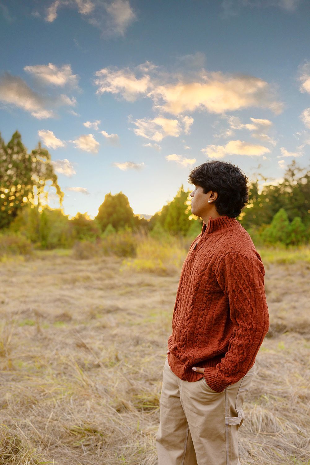 A man in a red sweater is standing in a field with his hands in his pockets