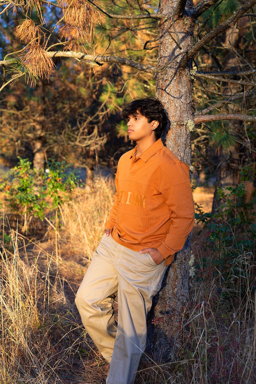 A young man is leaning against a tree in the woods