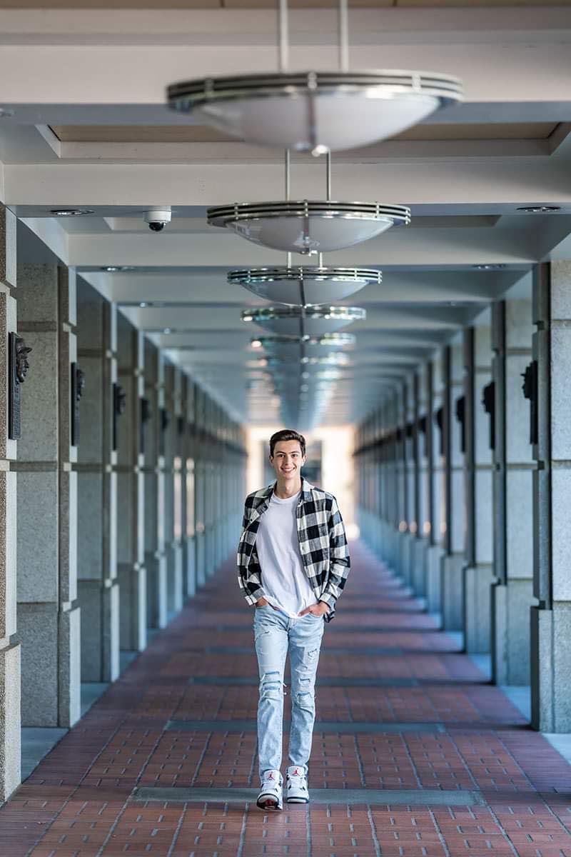 A young man is standing in a long hallway with his hands in his pockets