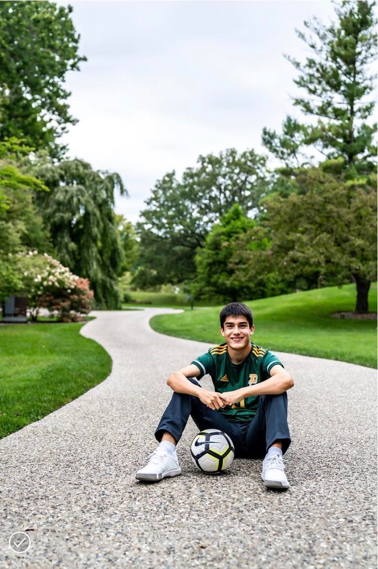 A young man is sitting on the side of a road with a soccer ball