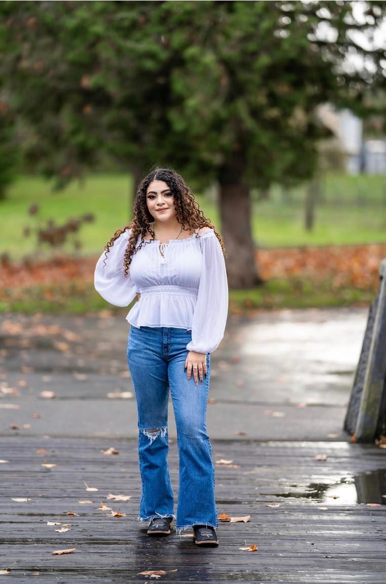 A woman in a white top and blue jeans is standing on a wet sidewalk
