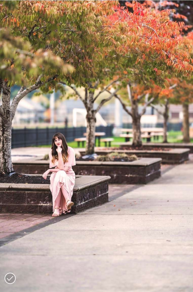 A woman is sitting on a bench under a tree in a park