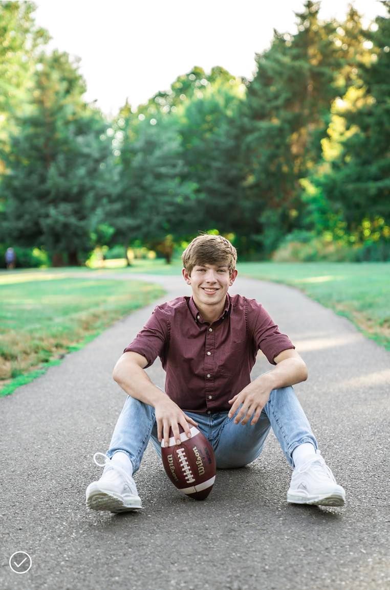 A young man is sitting on the sidewalk holding a football
