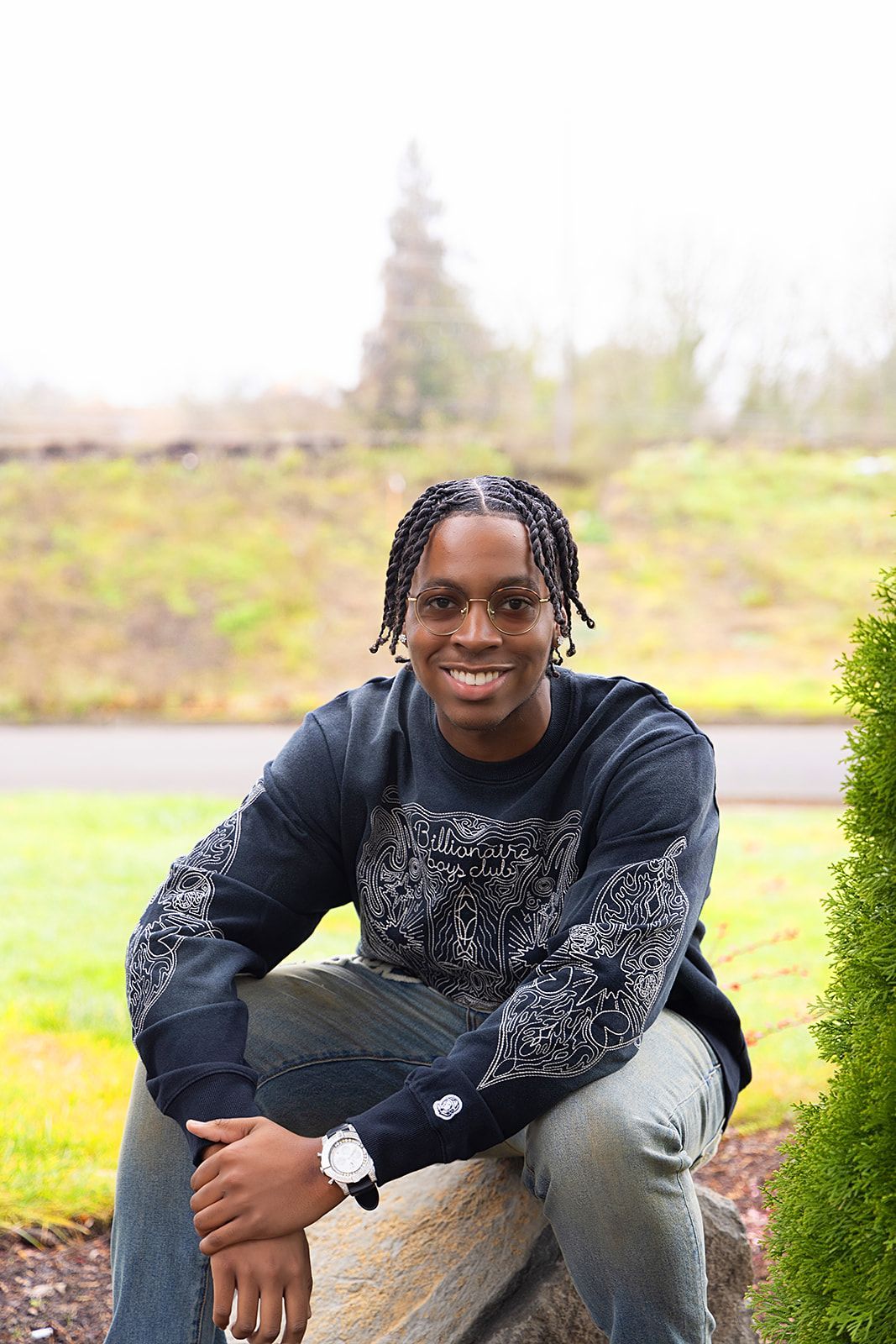 A man is sitting on a rock wearing glasses and a watch.