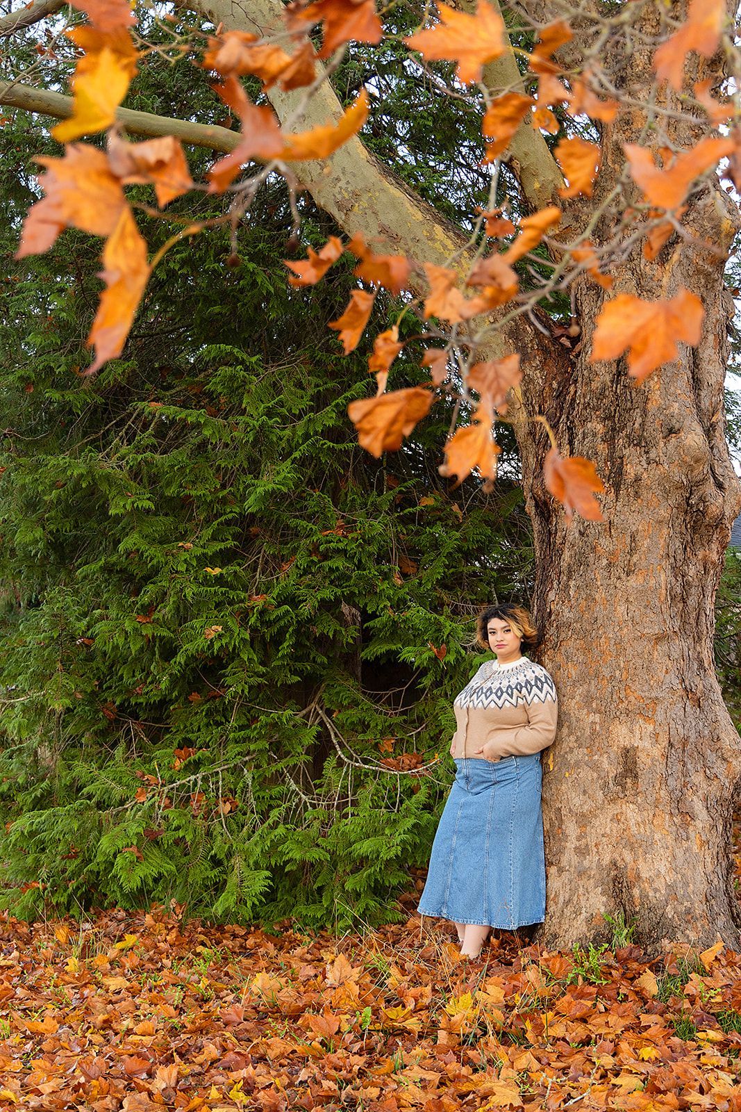 A woman is leaning against a tree covered in leaves.