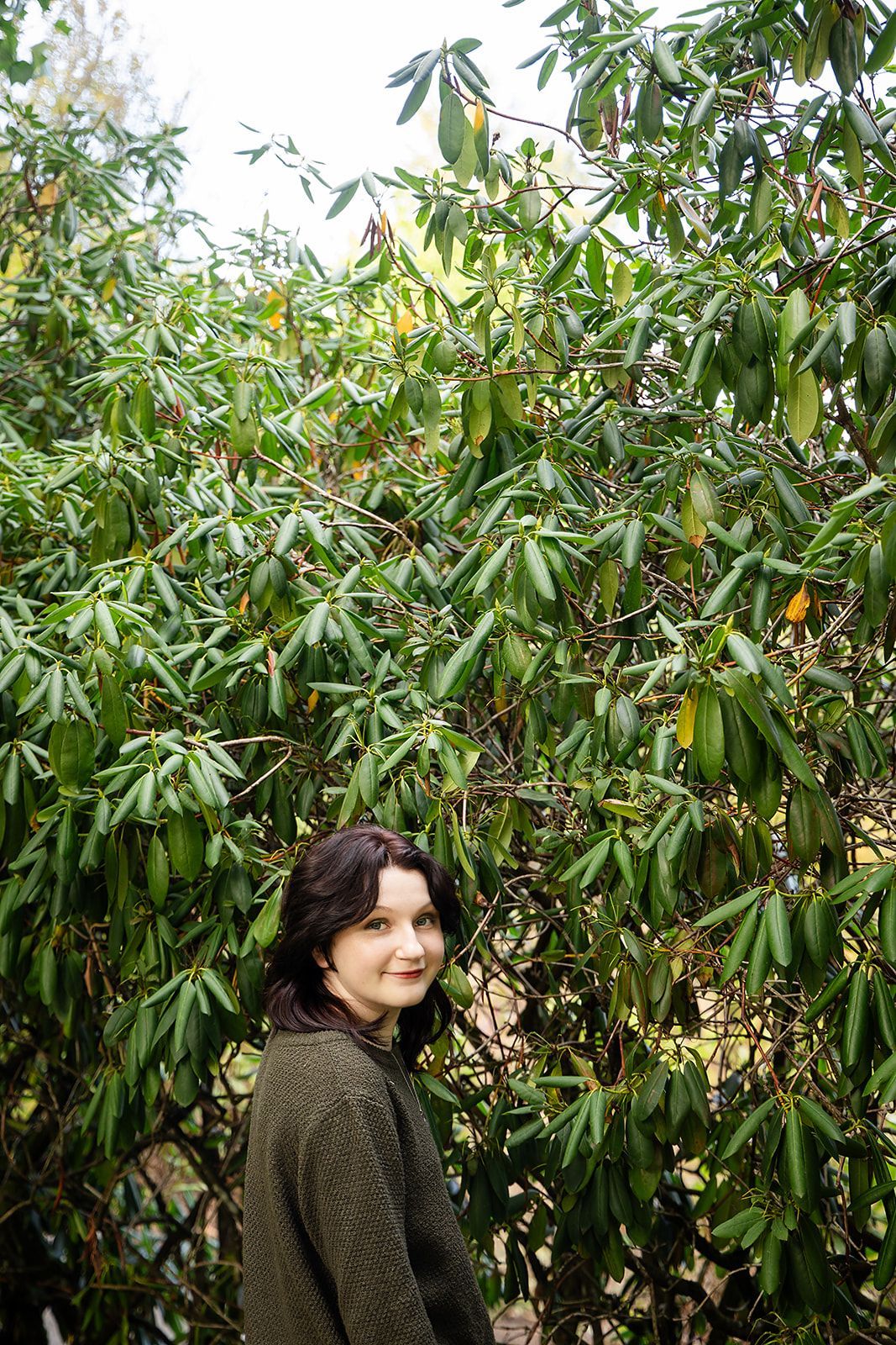 A woman is standing in front of a tree with lots of leaves.