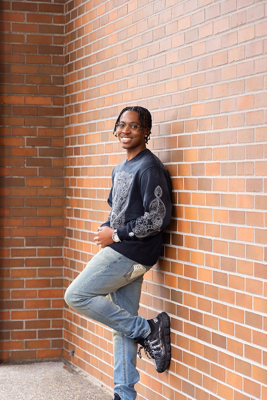 A young man is leaning against a brick wall.