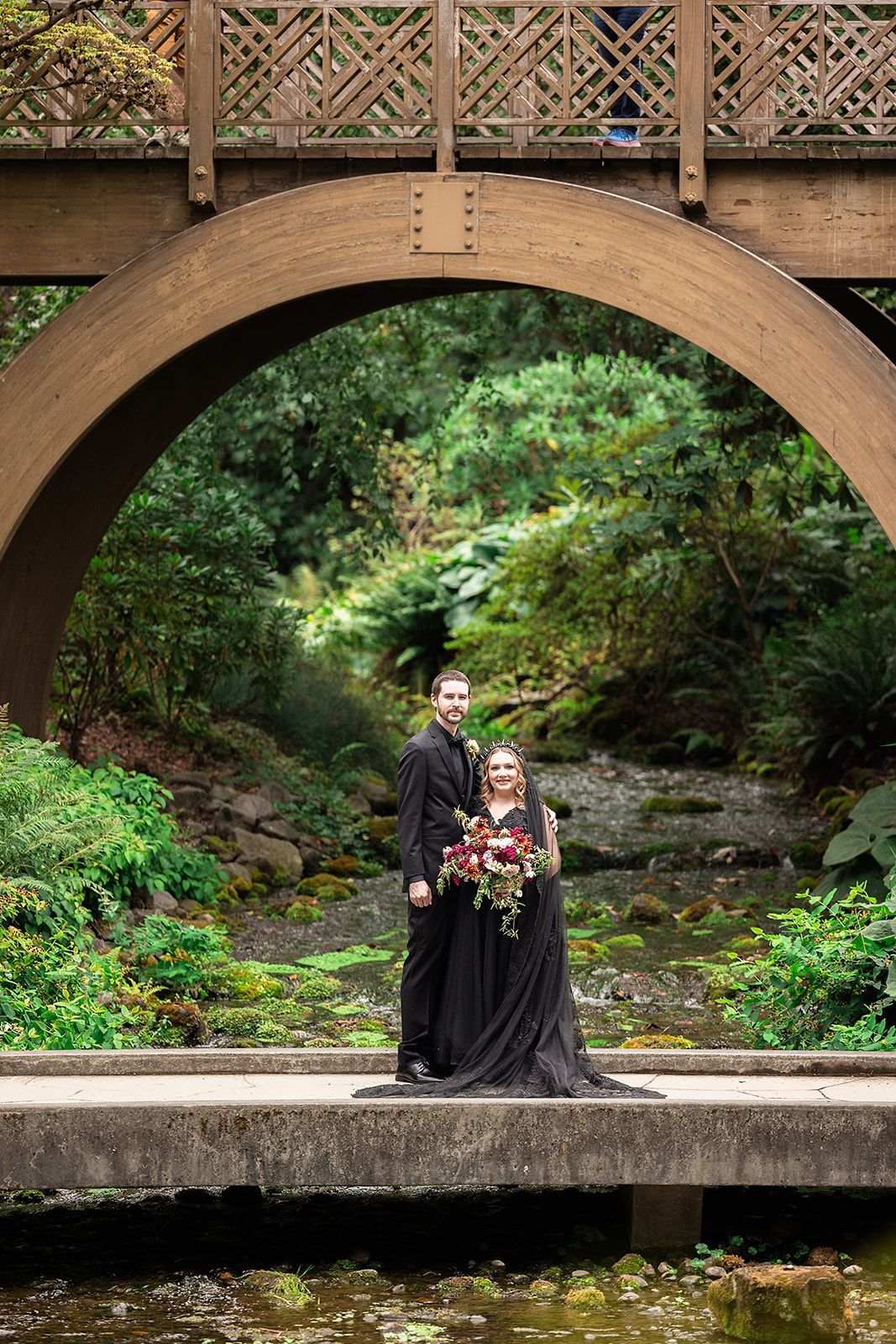 A bride and groom are standing on a bridge over a river