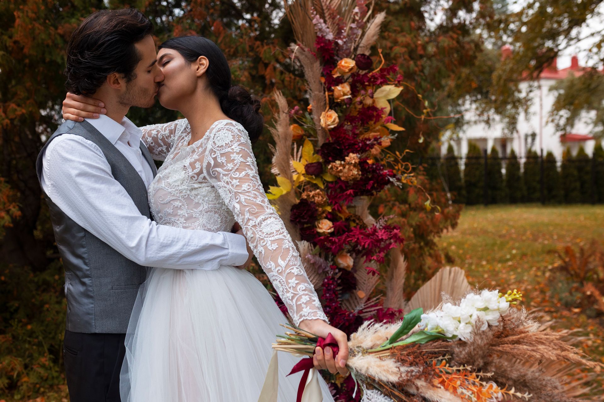 A bride and groom are kissing in front of a tree holding a bouquet of flowers