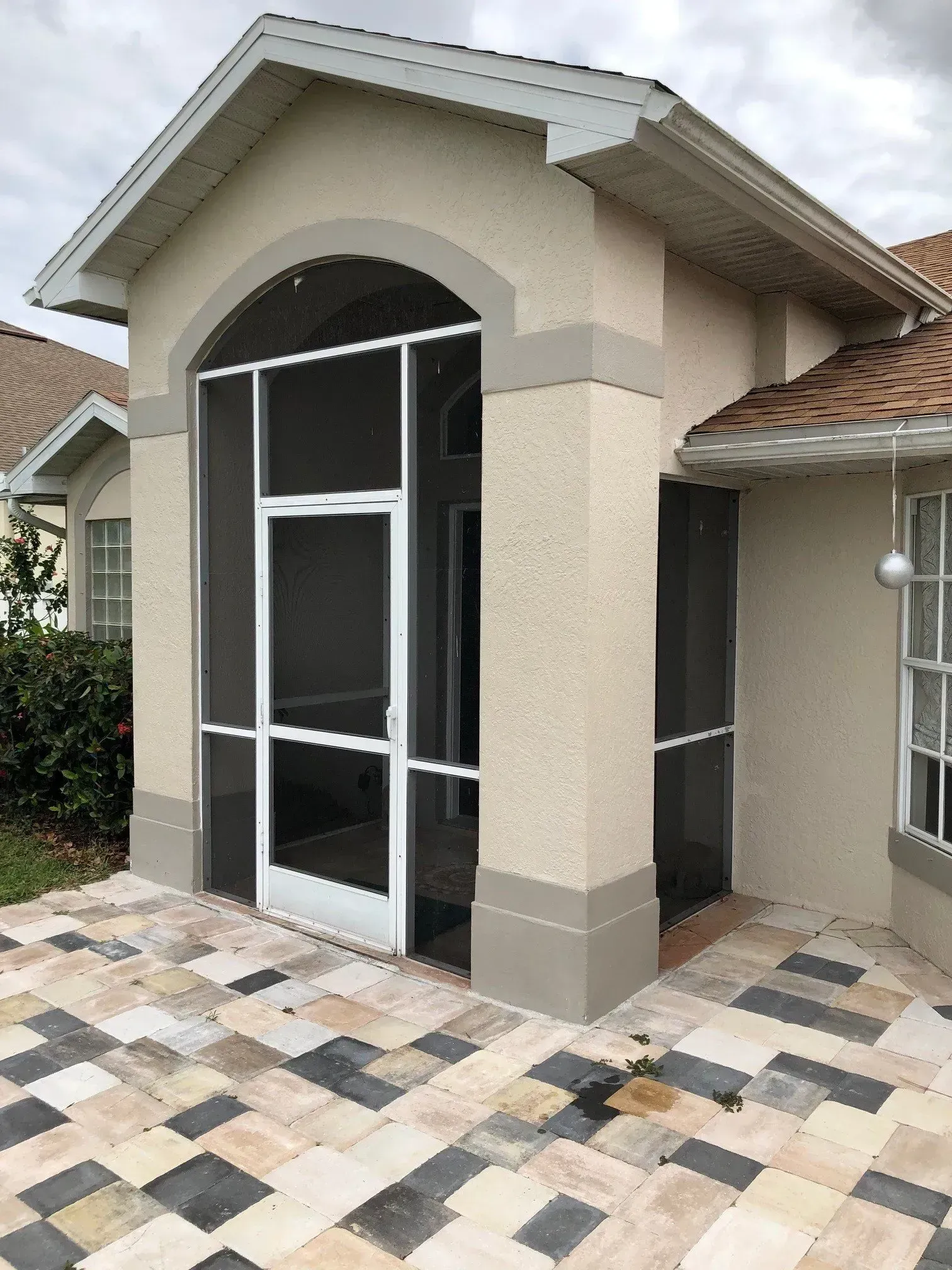 Screened-in patio with white frame door and windows, tan walls, and patterned brick floor.