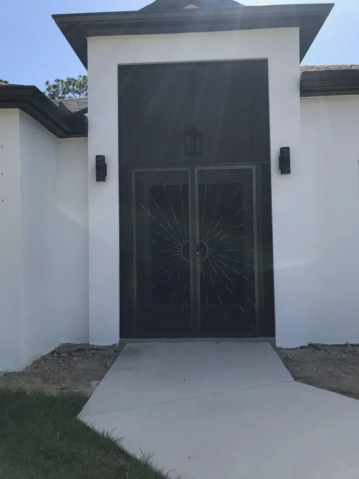 White house entrance with double dark doors, sconces, and a concrete path.