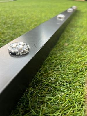 Metal ruler with water droplets lying on green grass outdoors.