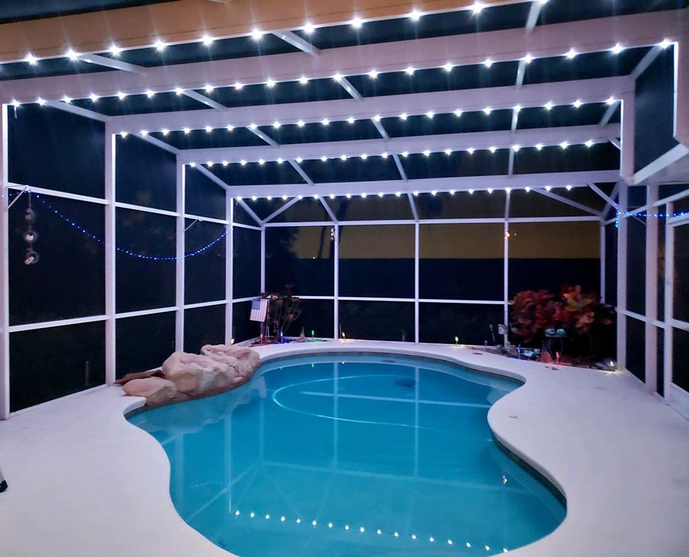 Covered backyard pool at night with white patio and string lights overhead.
