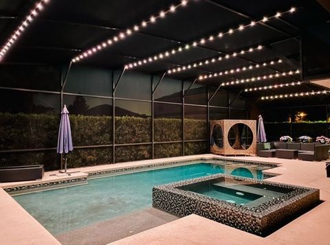 Indoor screened pool area with lit ceiling, hot tub, lounge chairs, and closed patio umbrella.