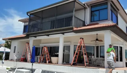 Two-story house exterior under construction with ladders, workers, and white stucco walls