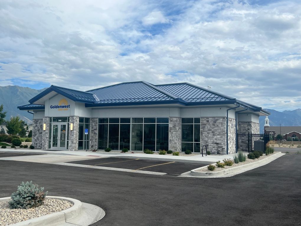 Modern bank building with gray brick exterior, large windows, blue roof, and mountain backdrop.