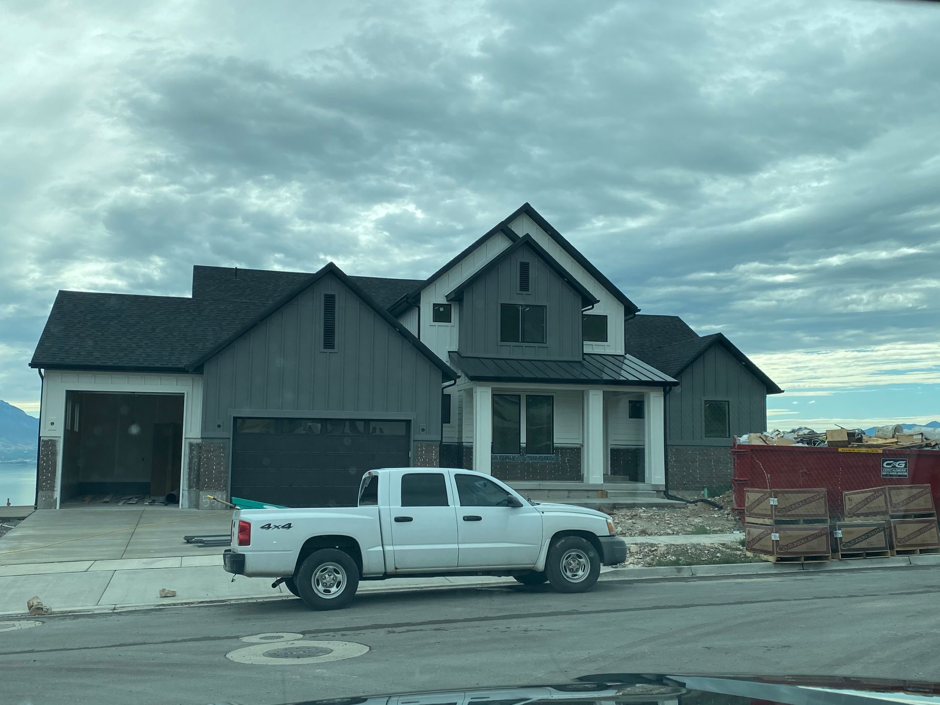 White pickup truck parked in front of a new house with dark gray siding and black roof under a cloudy sky.