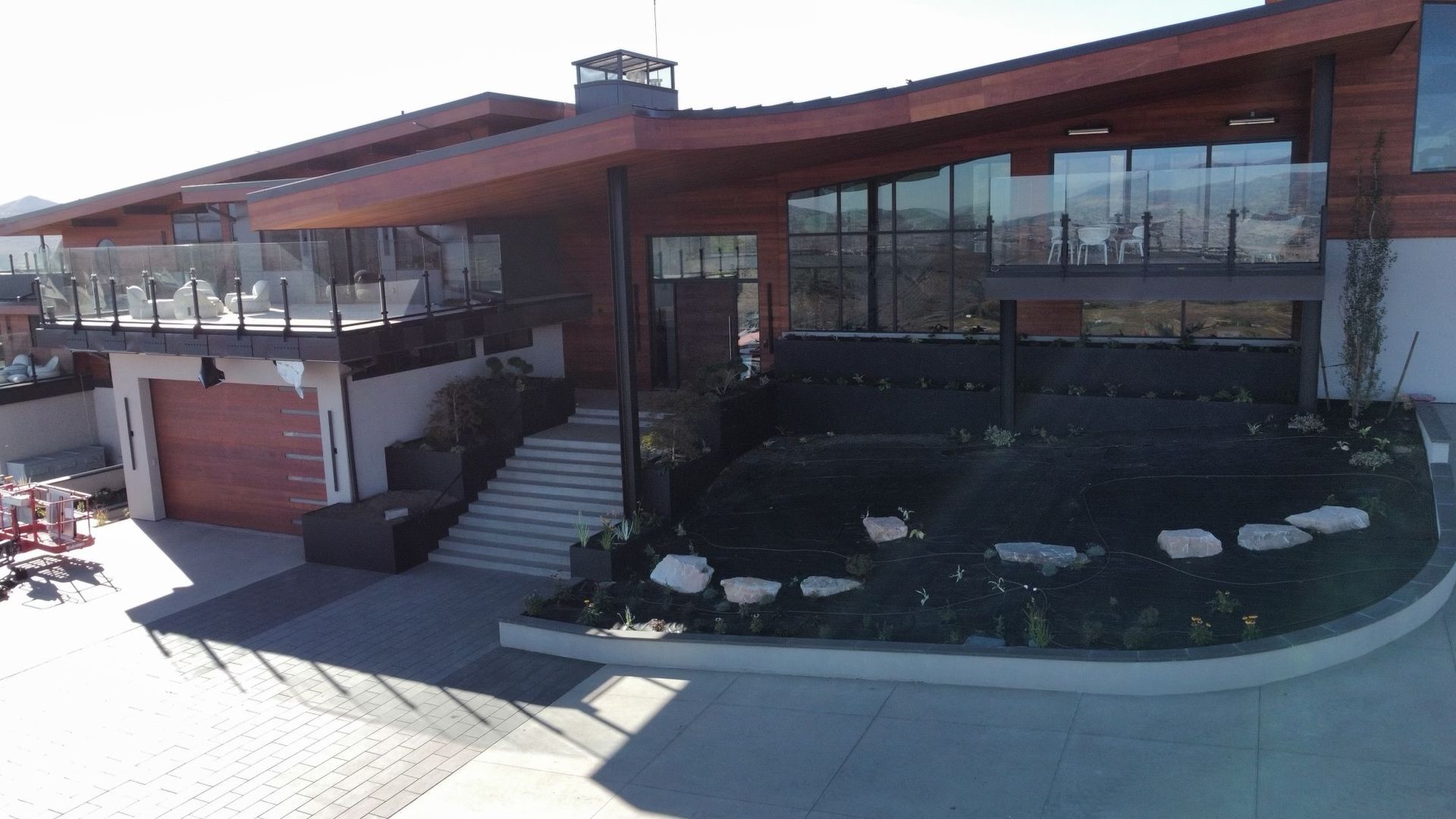 Modern house with wood siding, glass windows, and a balcony. Landscaping in front.