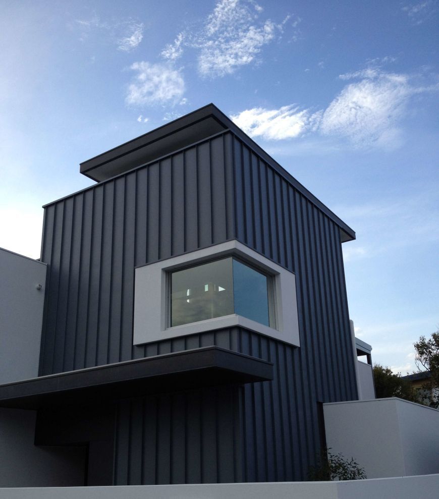 Modern building with gray vertical panel siding, white window trim, and a blue sky.