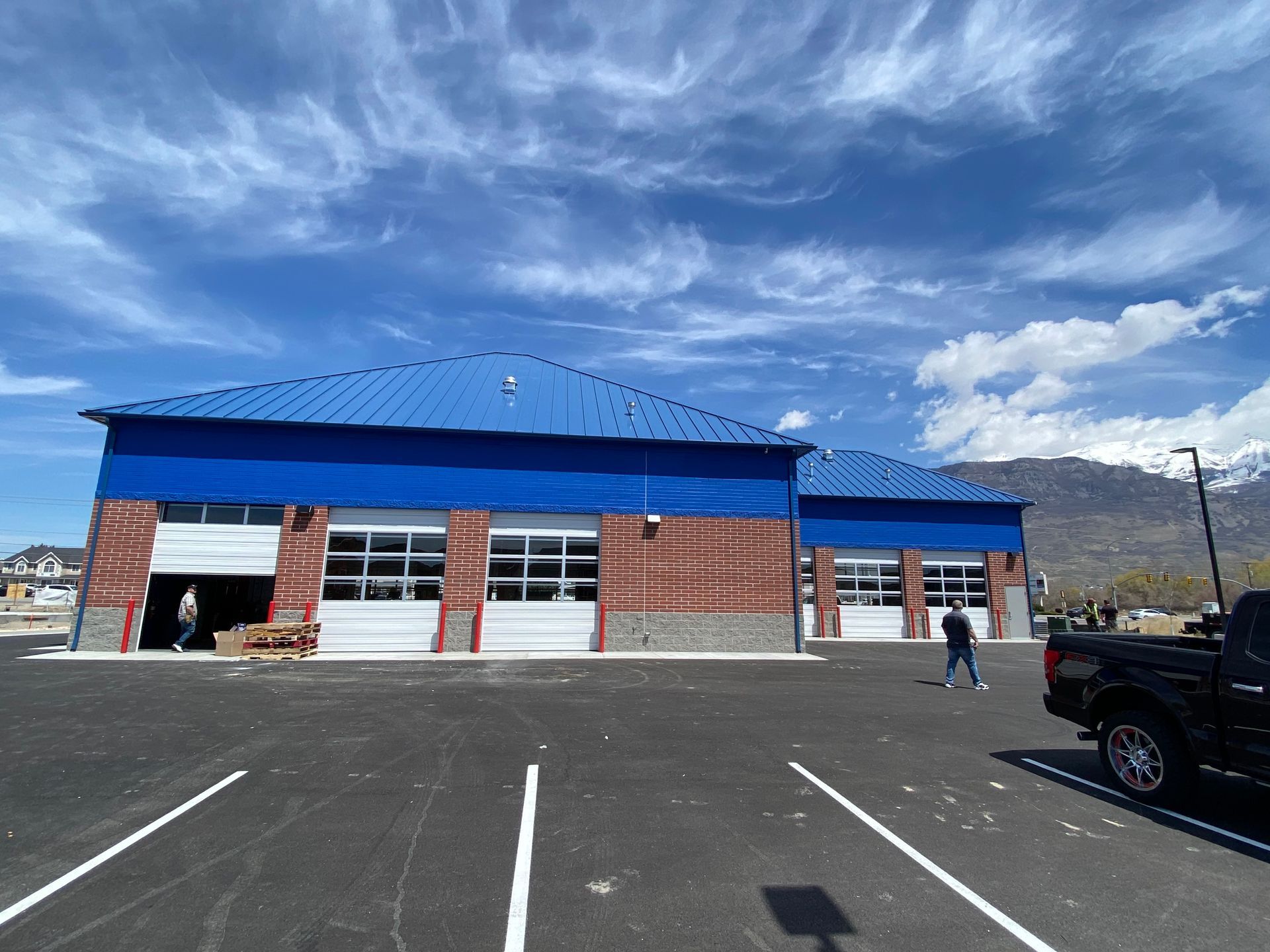 Blue building with three garage doors; a black truck in the parking lot. Bright blue sky with clouds.