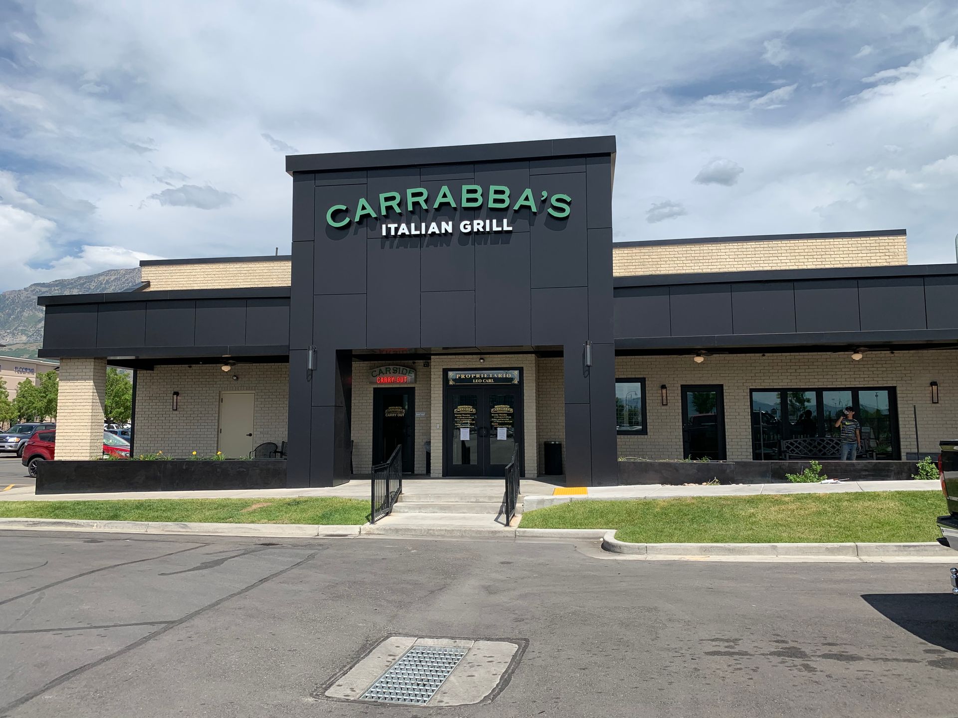 Carrabba's Italian Grill restaurant exterior, dark gray facade, green sign, steps leading to the entrance, cloudy sky.