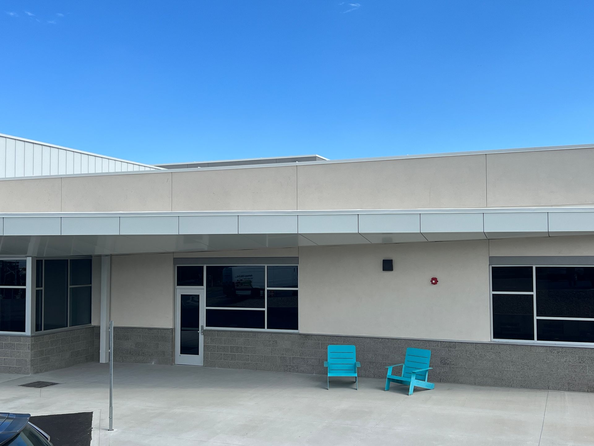 Building exterior with windows, door, light blue chairs, and a blue sky.