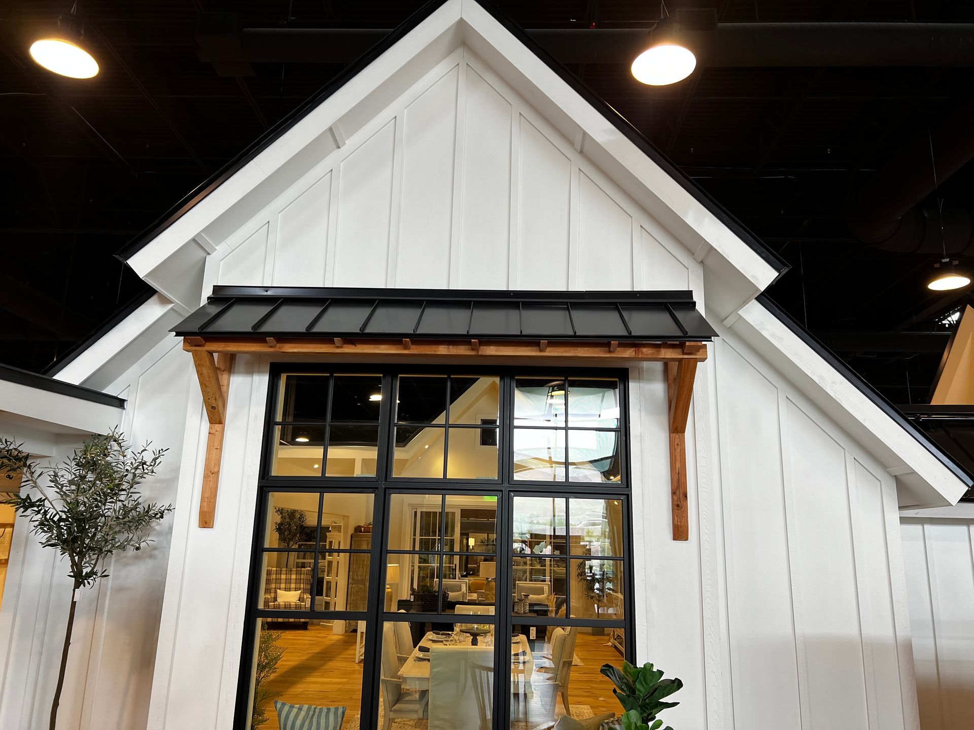 White farmhouse-style building with a black-framed window and a black awning supported by wooden brackets.