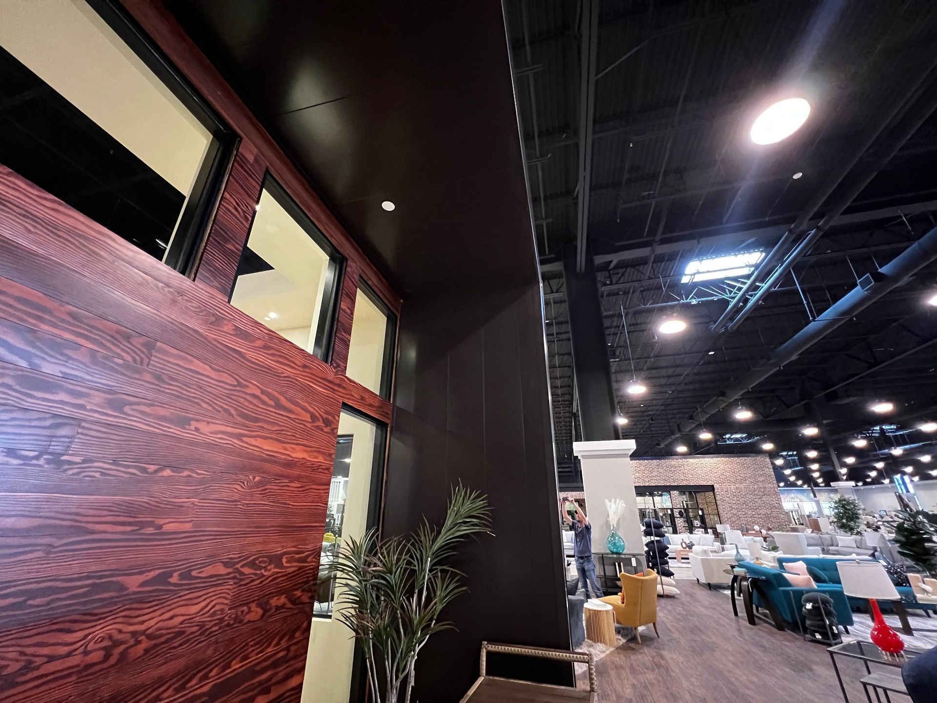 Interior view of a furniture store. Dark wood paneling and windows on the left. Store is brightly lit.