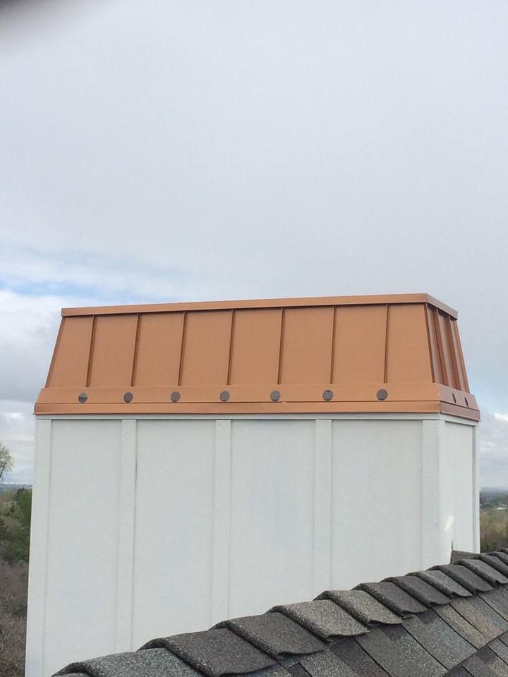 Copper chimney cap on white chimney, set against a cloudy sky.