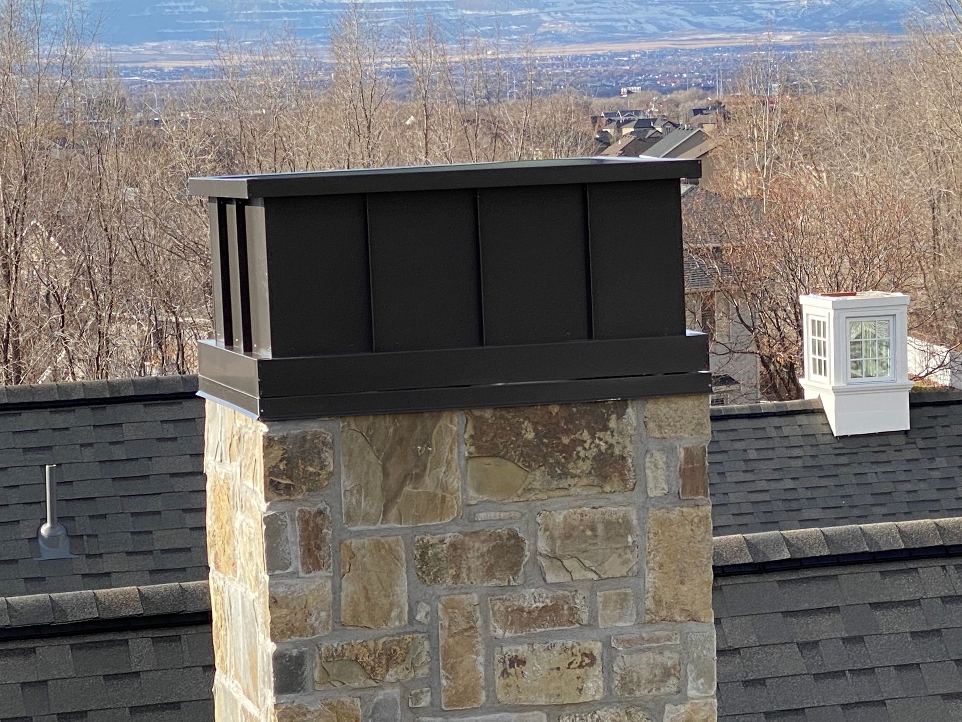 Stone chimney with a dark metal cap on a rooftop.