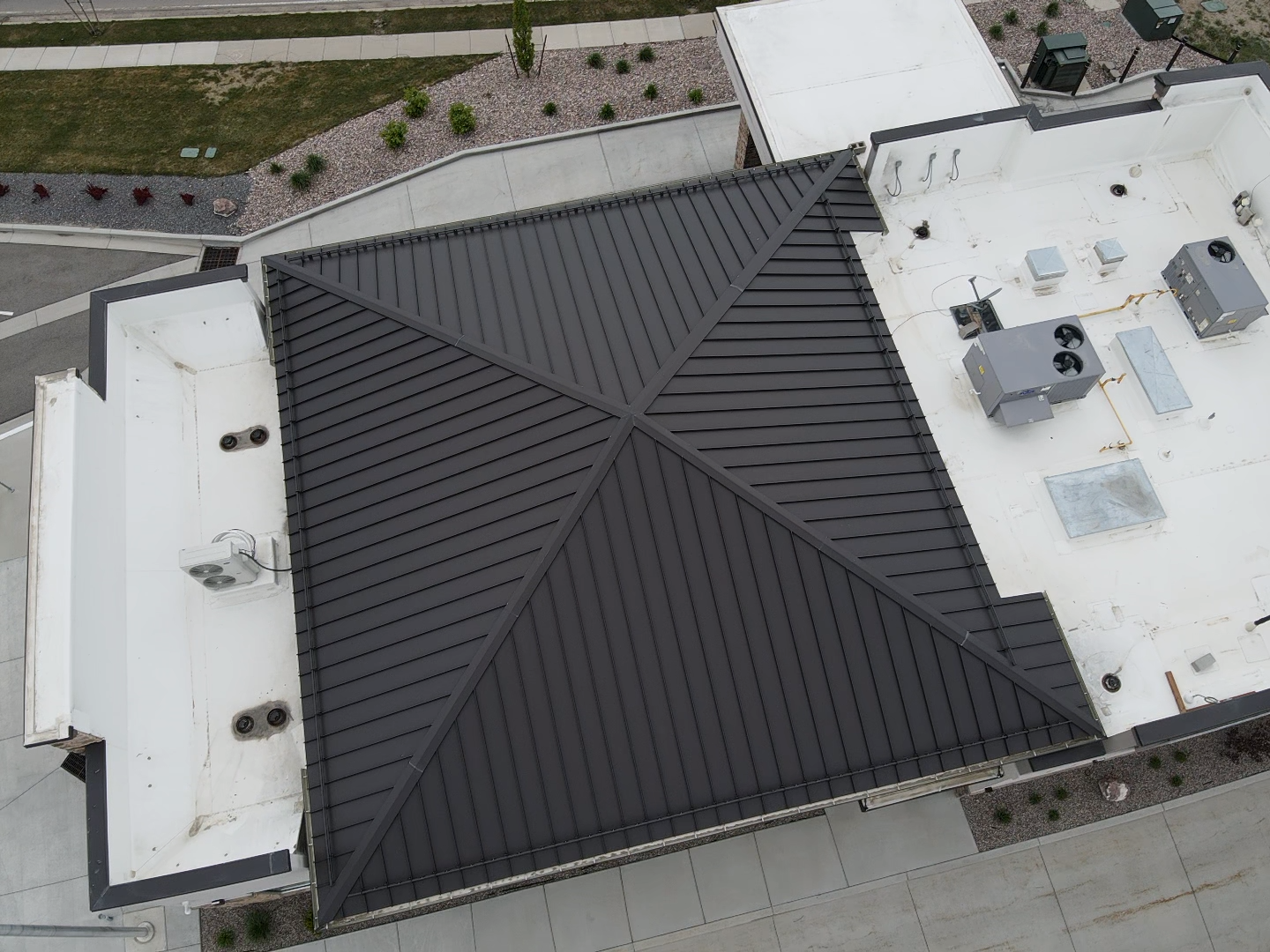 Overhead view of a building with a dark metal roof and white flat roof sections.